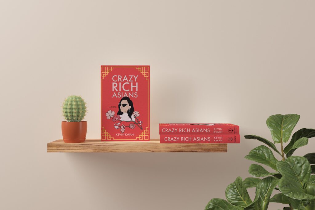 A red book, "Crazy Rich Asians," stands prominently on a wooden shelf, while two other books lie adjacent on the same shelf.
