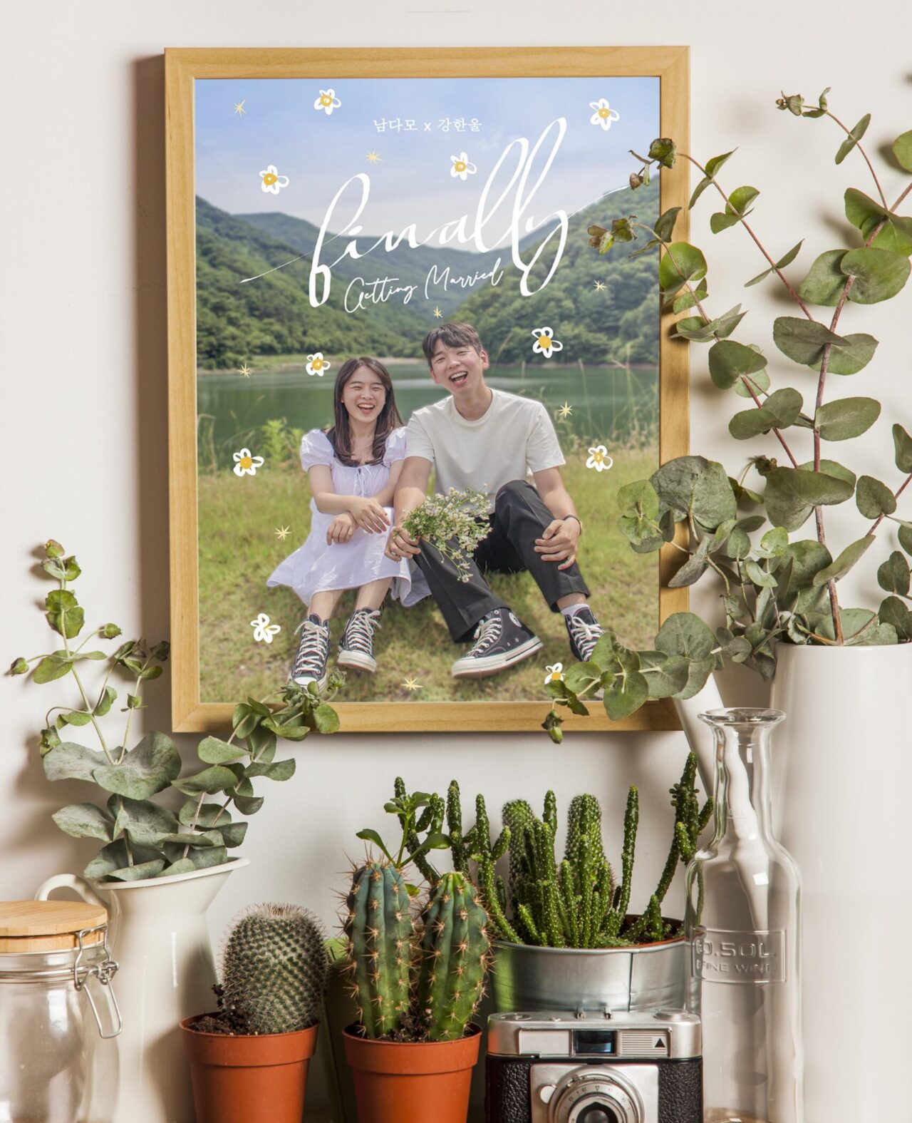 A couple is sitting on the ground in a frame, and the frame is hanging on the wall. There are a lot of plants surrounding the frame.