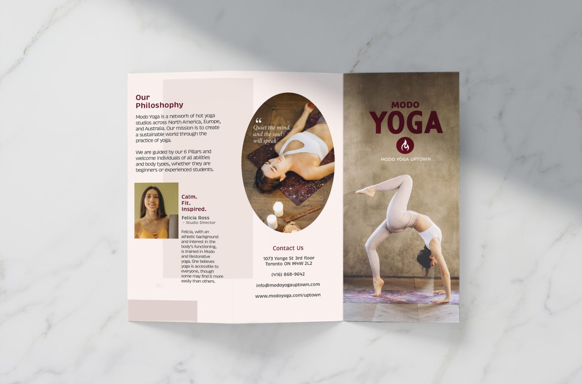 A tri-fold brochure is elegantly displayed on a marble background, casting subtle shadows that enhance its presence. The brochure unfolds to reveal captivating details about Modo Yoga studio, promising a glimpse into its offerings and ambiance.