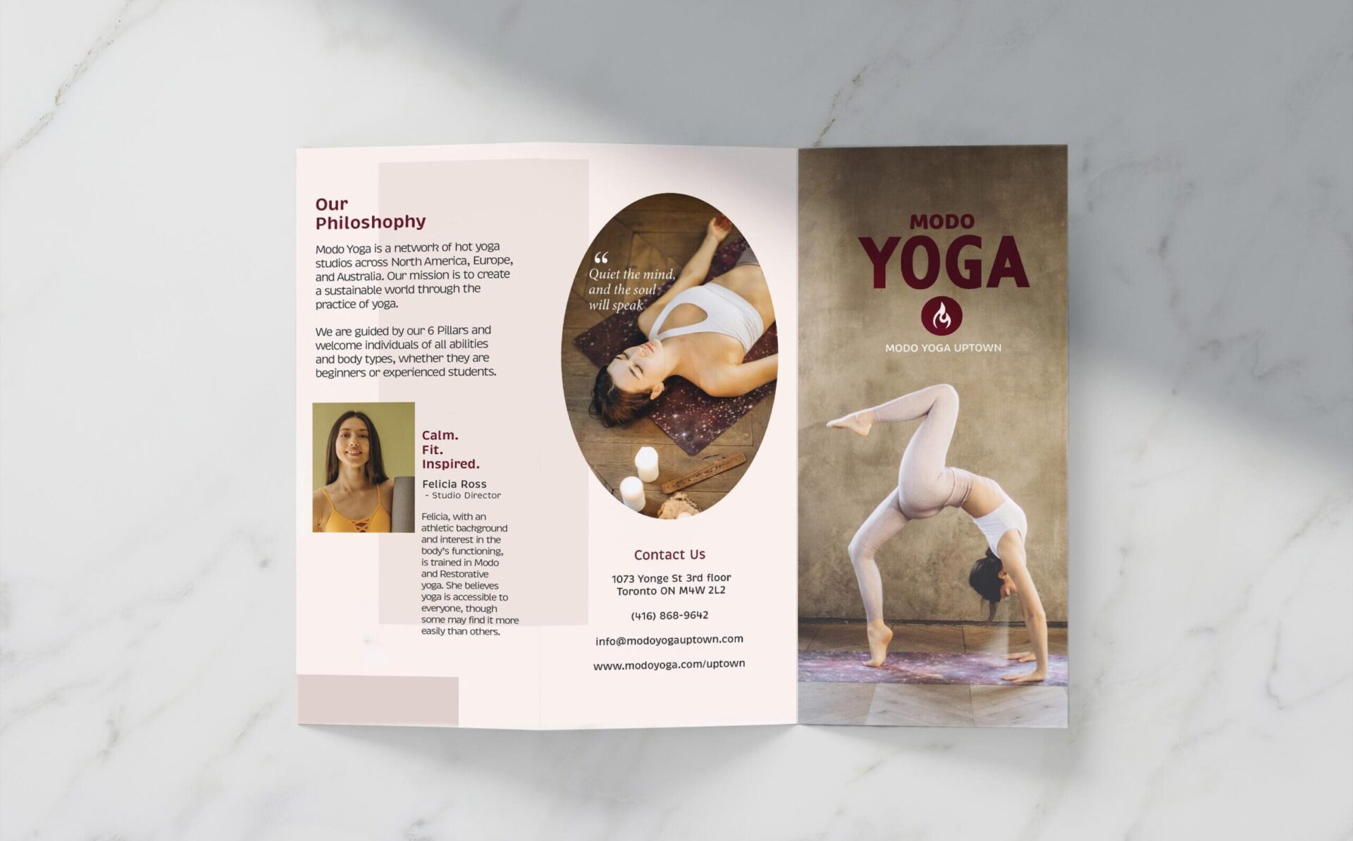 A tri-fold brochure is elegantly displayed on a marble background, casting subtle shadows that enhance its presence. The brochure unfolds to reveal captivating details about Modo Yoga studio, promising a glimpse into its offerings and ambiance.